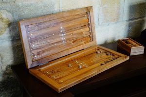 Coffret de backgammon en bois ouvert sur un meuble sombre, flèches marquetées et pions rangés dans une petite boîte