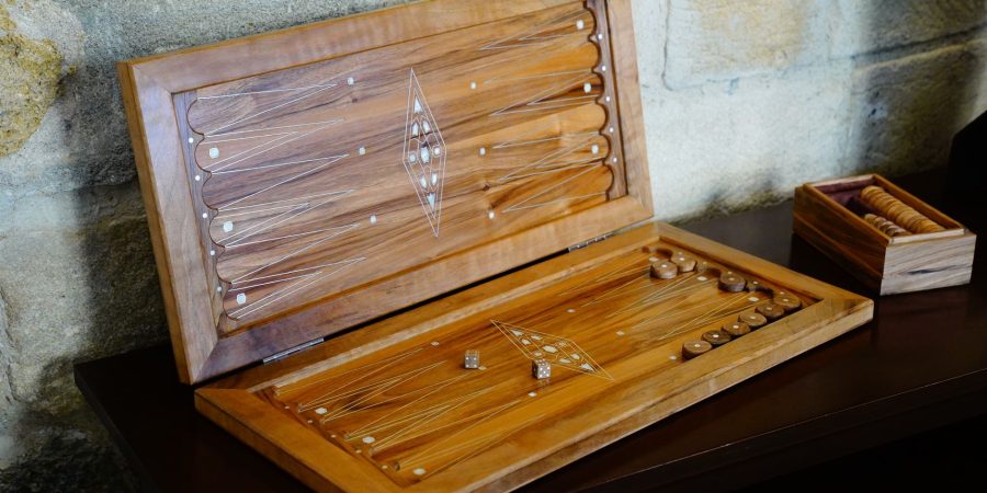 Coffret de backgammon en bois ouvert sur un meuble sombre, flèches marquetées et pions rangés dans une petite boîte