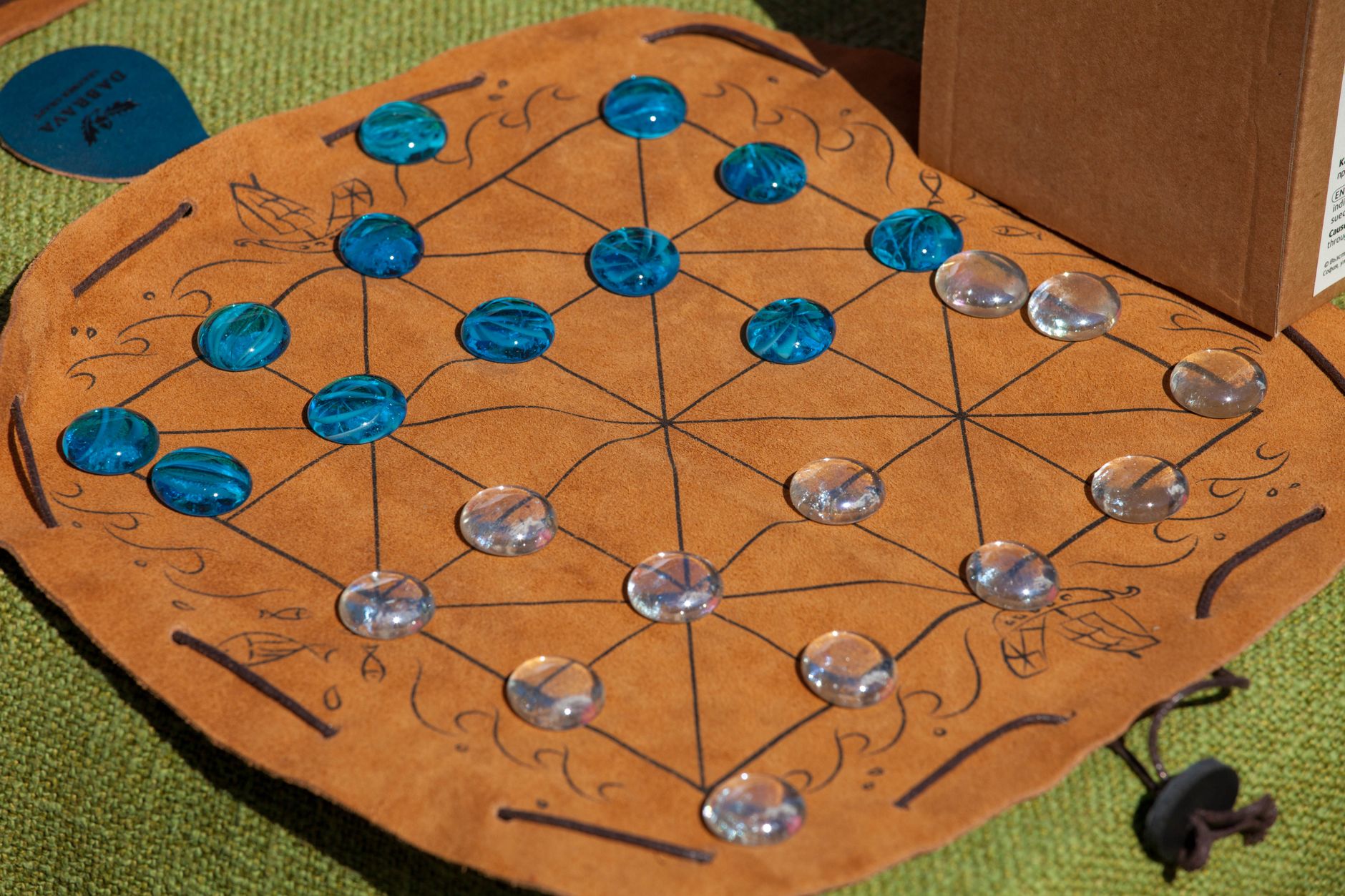 Plateau du moulin avec diagonales sur un tapis en cuir, avec des pions en verre bleus et transparents