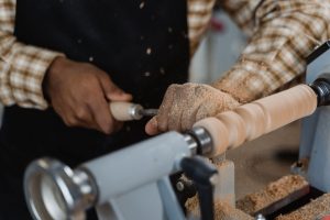 Mains d'un artisan tournant une pièce de bois allongée sur un tour, copeaux sur le banc