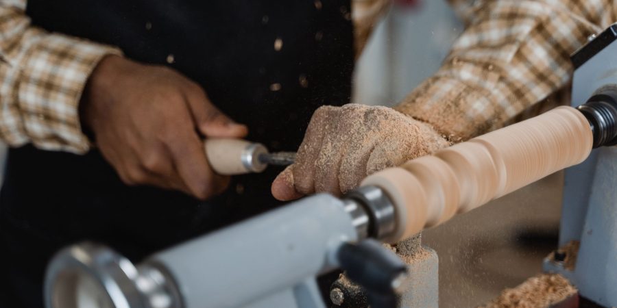 Mains d'un artisan tournant une pièce de bois allongée sur un tour, copeaux sur le banc