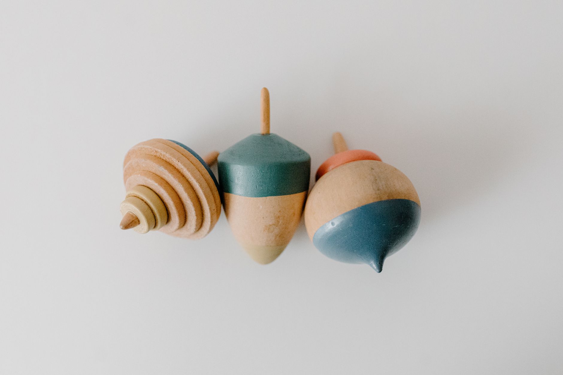 Trois toupies en bois tourné, dont deux peintes en vert, bleu et orange, sur fond blanc